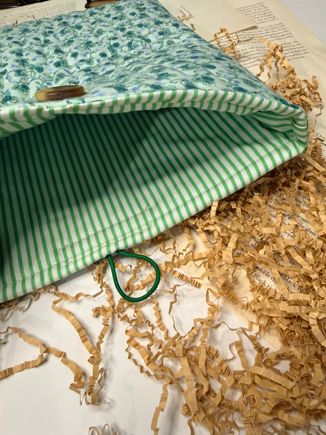 quilted book sleeve in Green and white striped fabric with a button on top of crumpled paper