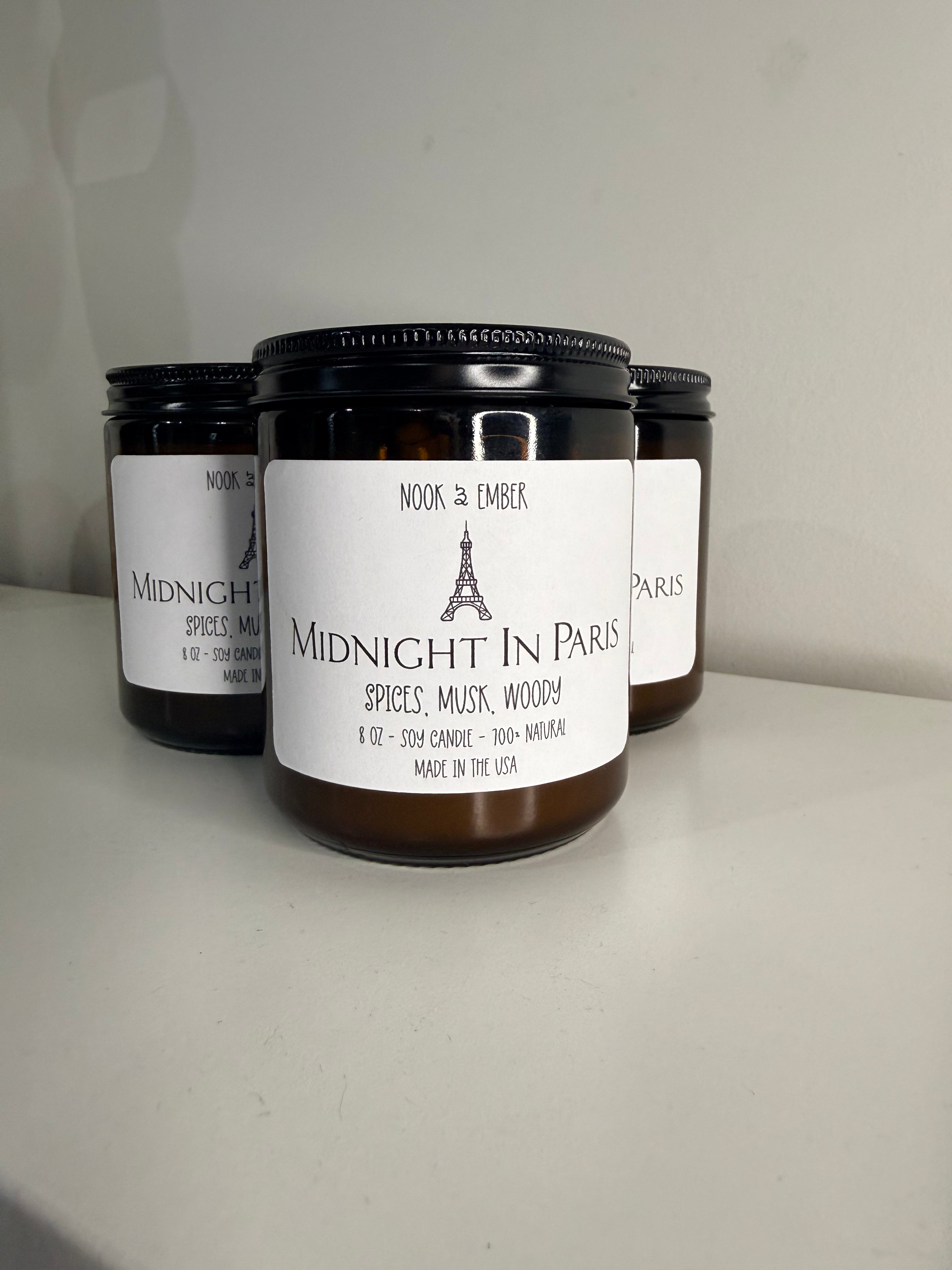 Three candles in amber glass jars with white labels with eiffel tower on them.