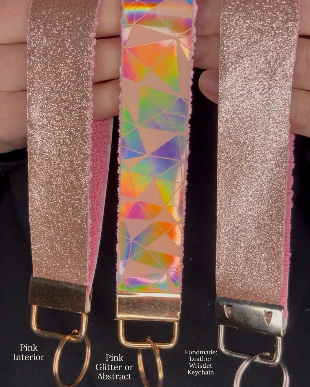 Pink glitter and pink abstract wristlet keychains held in hands on black background