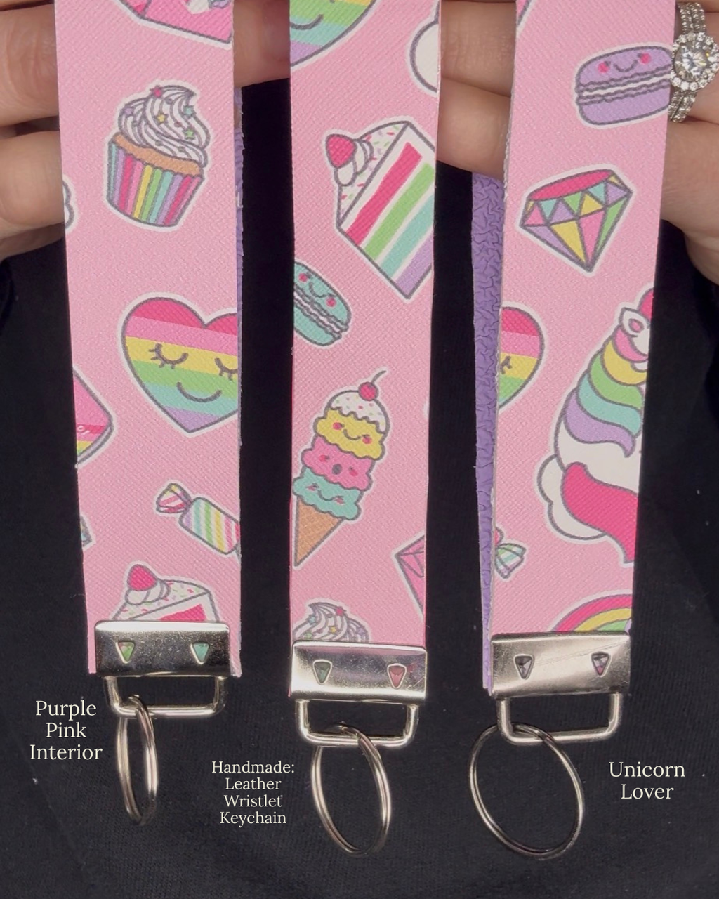 Pink wristlet keychain with colorful unicorn and food designs held by a hand against a black background.